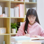 Young Asian female student studying at home, writing notes and learning Japanese online in a bright study room