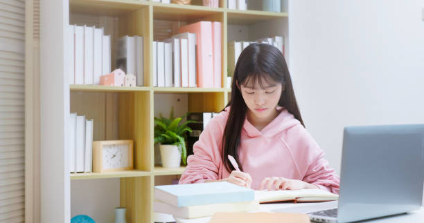 Young Asian female student studying at home, writing notes and learning Japanese online in a bright study room